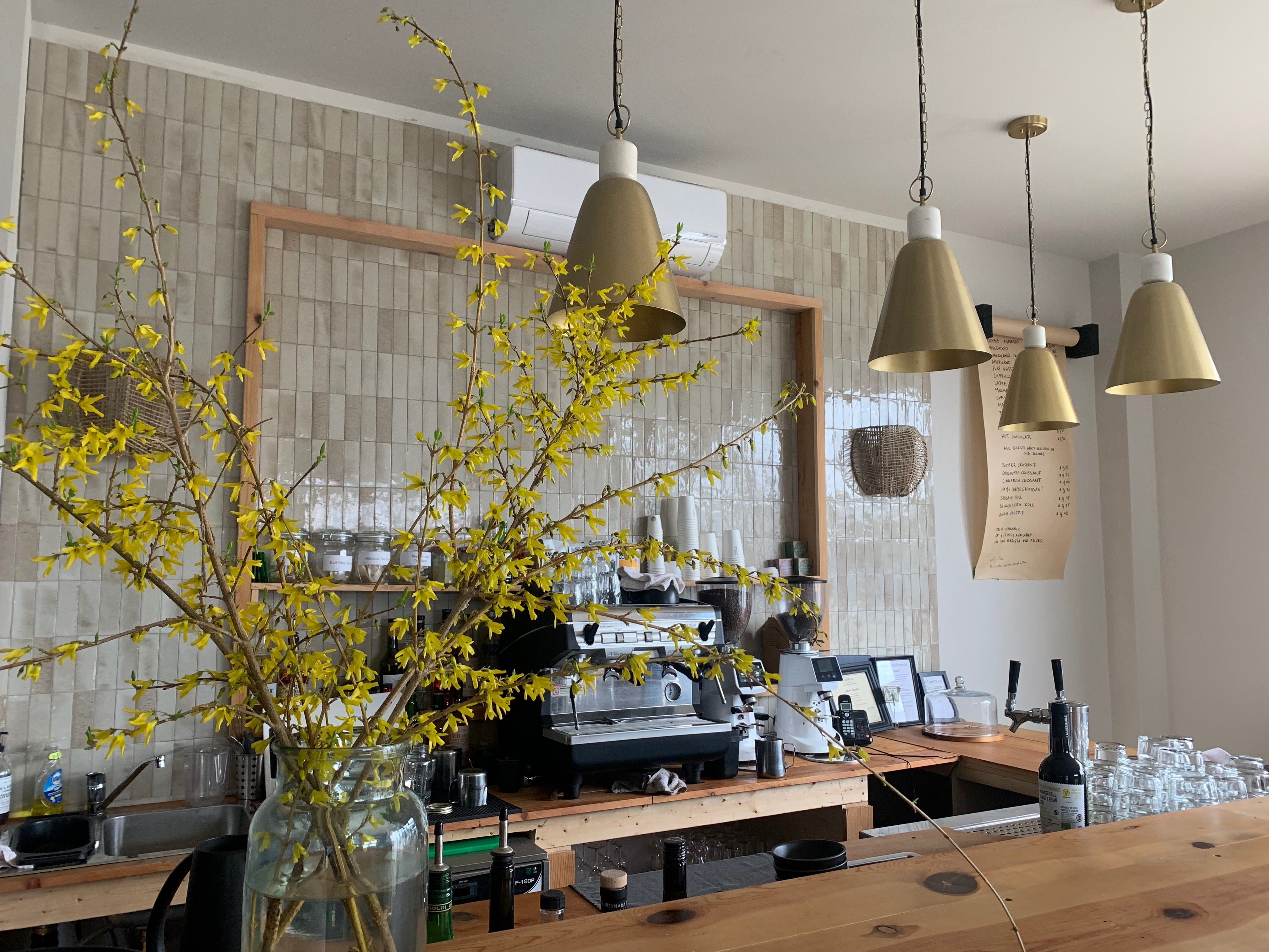 Modern kitchen with yellow flowers in a vase, pendant lights, and a coffee machine.